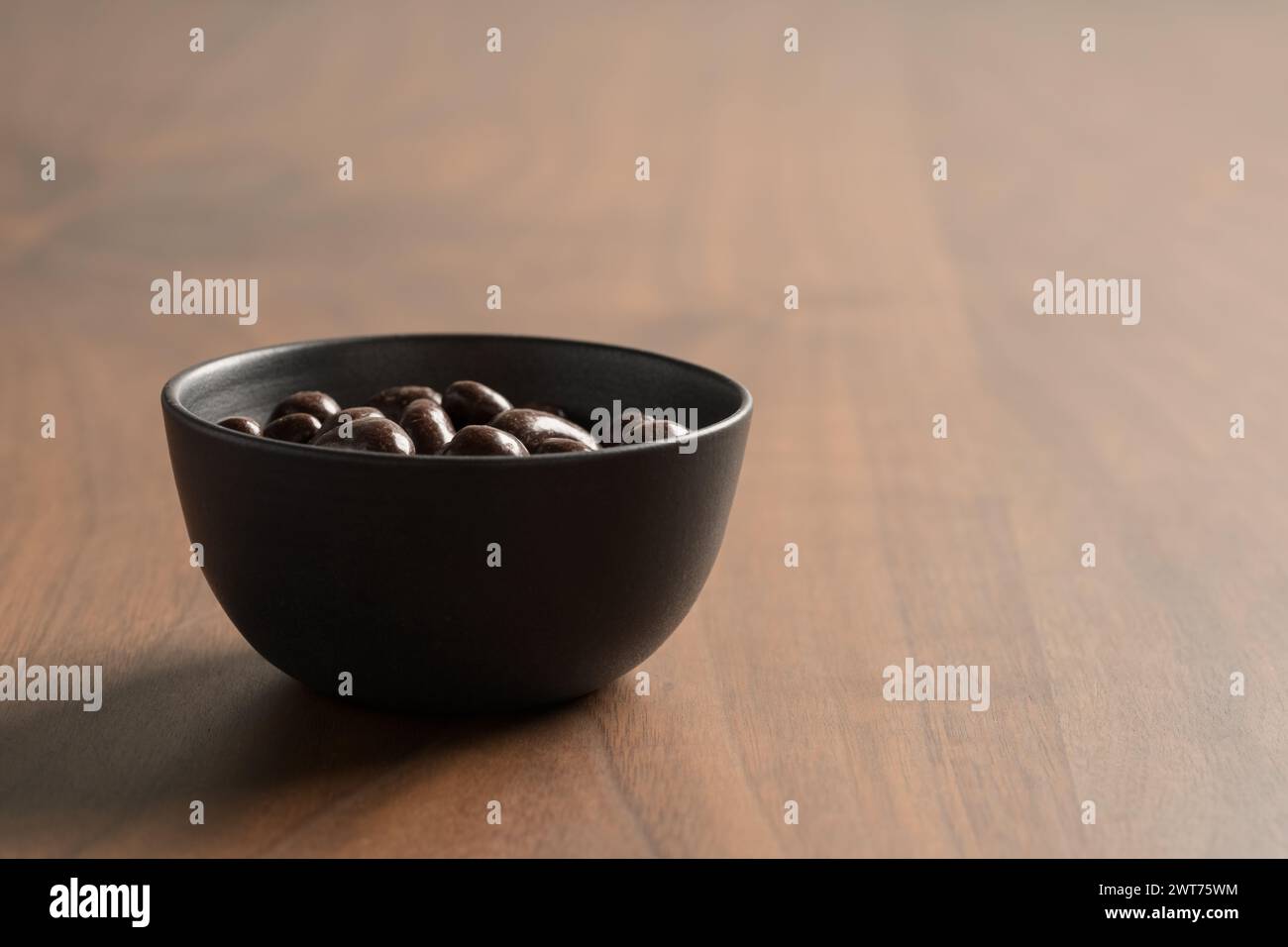 Anacardi ricoperti di cioccolato in una ciotola su un tavolo di legno, messa a fuoco superficiale Foto Stock