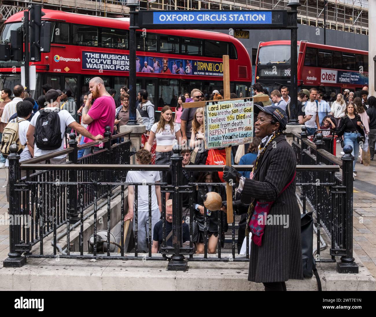Una predicatrice femminile di strada fuori da una trafficata stazione della metropolitana di Oxford Circus tiene un cartello di Gesù mentre i pendolari scendono nella stazione. Centro di Londra. Foto Stock