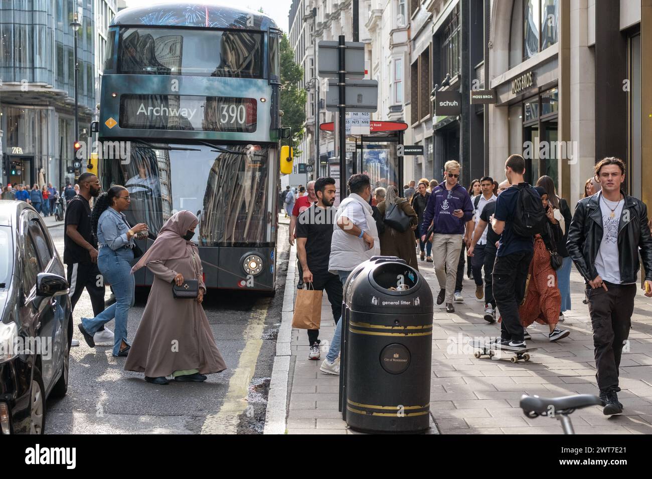 L'autobus 390 è a una fermata di Oxford Street, Londra. La scena è piena di pedoni che attraversano la strada e passano accanto ai negozi. Foto Stock