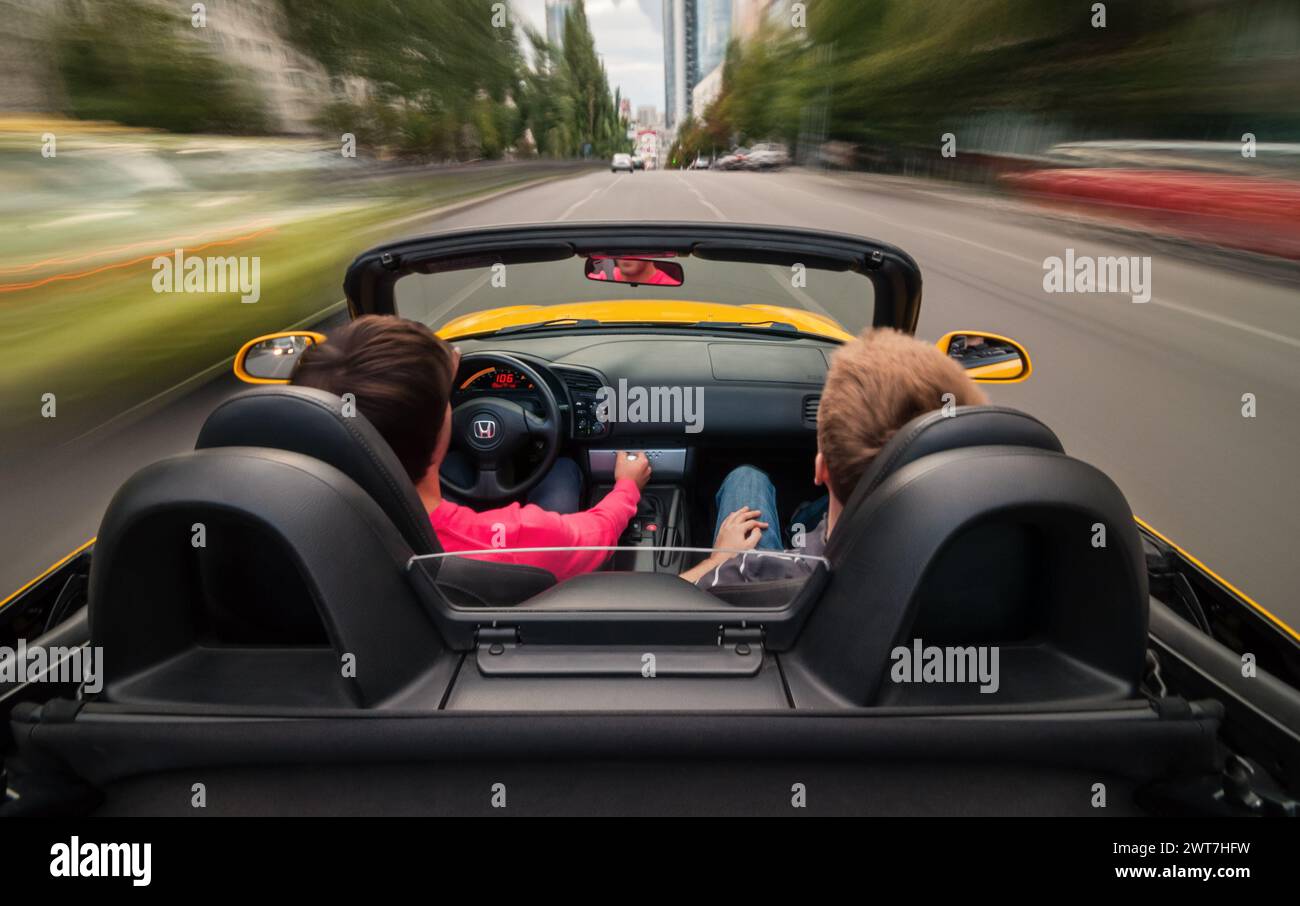 Guida veloce nel traffico urbano. Auto sportiva gialla con conducente e passeggeri che accelerano su strade trafficate in città. Senso di velocità. Foto Stock