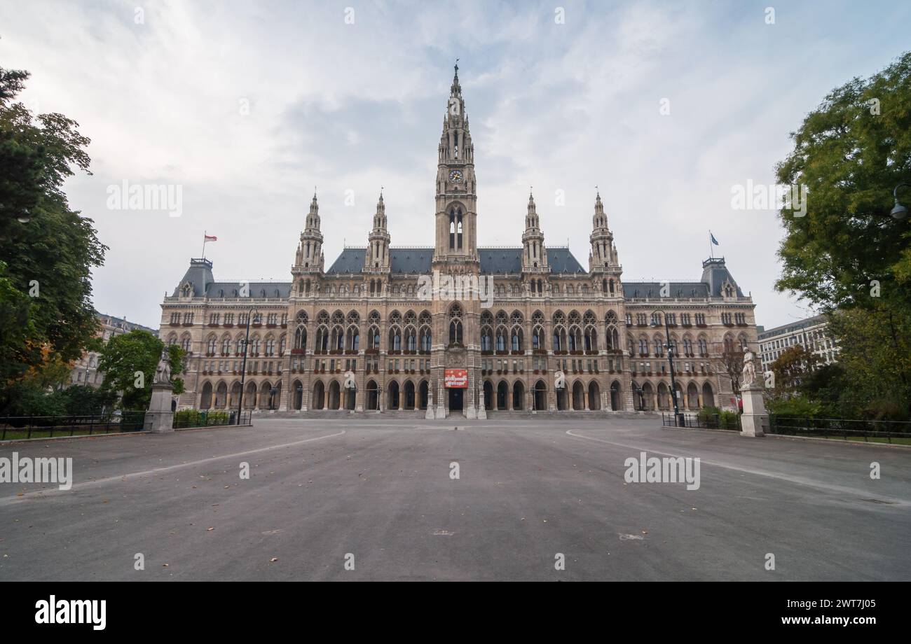 Vista simmetrica del Municipio di Vienna. Edificio neogotico Rathaus e piazza vuota di fronte ad esso, alberi verdi ai lati. Giornata nuvolosa. Foto Stock