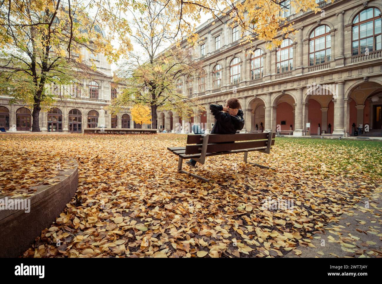 Uomo seduto su una panchina nel cortile dell'edificio principale dell'Università di Vienna. Edificio del tardo XIX secolo in stile rinascimentale italiano. Autunno. Foto Stock