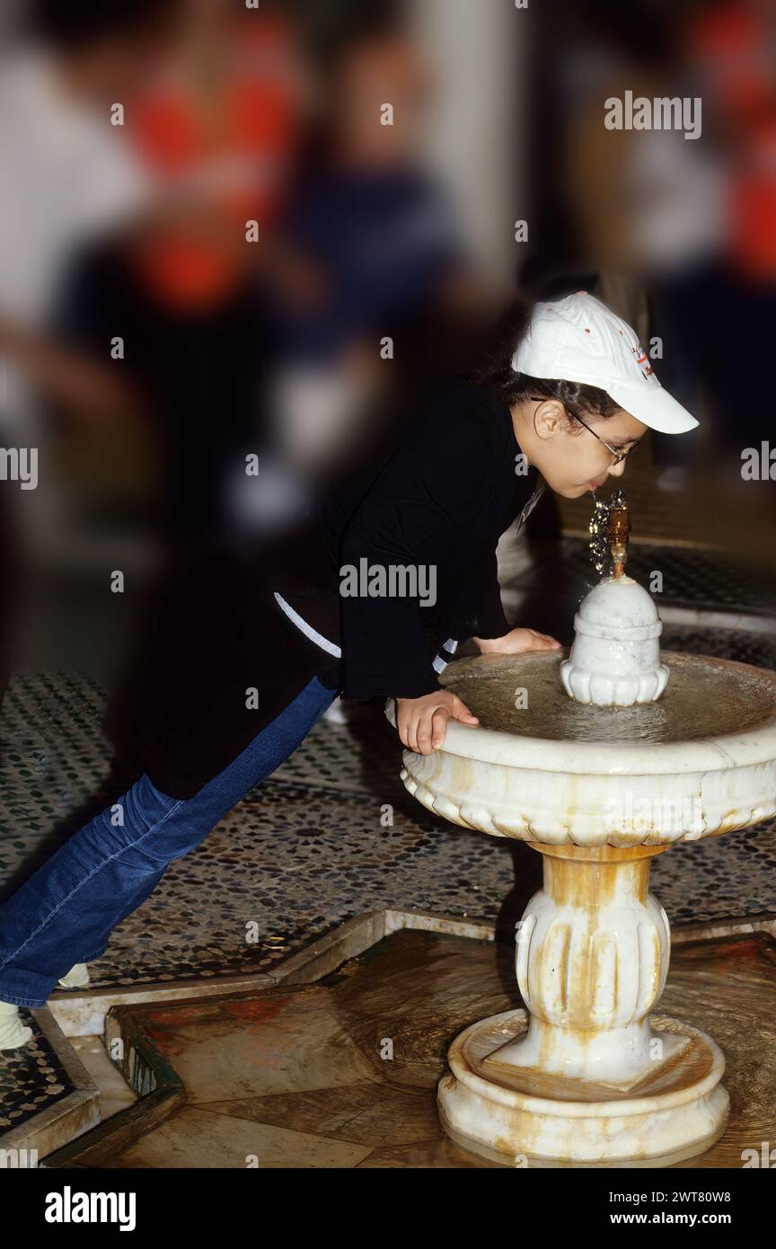 Meknes, Marocco. Lo scolaro beve dalla fontana del Mausoleo di Moulay Ismail. Foto Stock