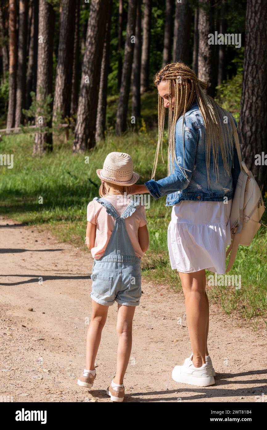 Una donna, madre, guida il suo bambino una bambina su un sentiero boscoso, inizia un viaggio di esplorazione della natura e cura materna, amore e cura dei genitori. Foto Stock