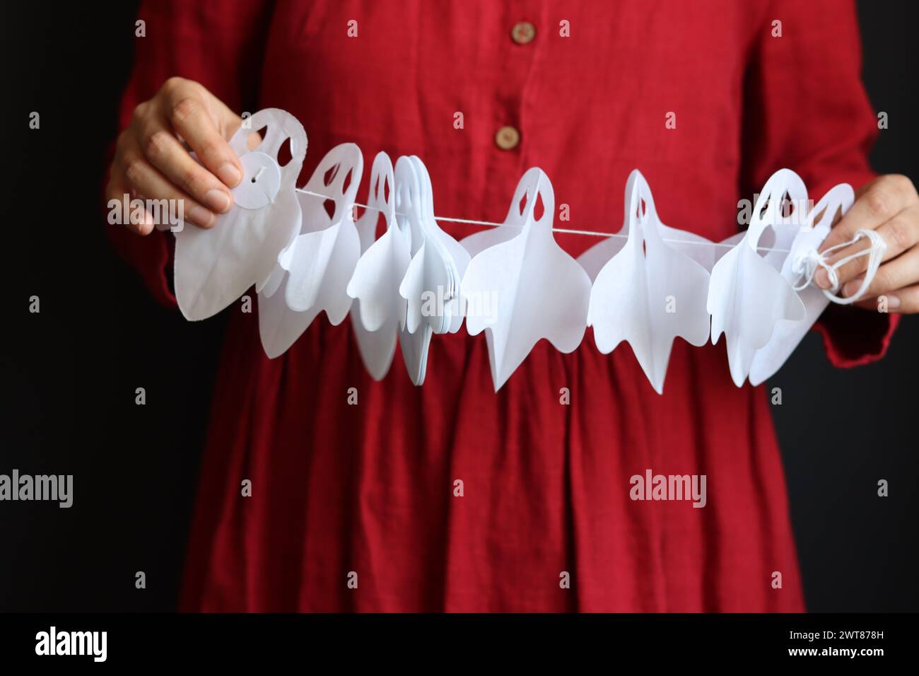 Una donna in abito rosso tiene in mano la carta bianca fantasma garland. Foto ravvicinata delle decorazioni di Halloween Foto Stock