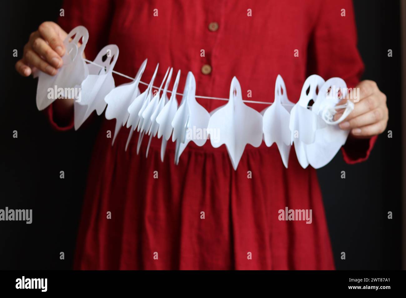 Una donna in abito rosso tiene in mano la carta bianca fantasma garland. Foto ravvicinata delle decorazioni di Halloween Foto Stock