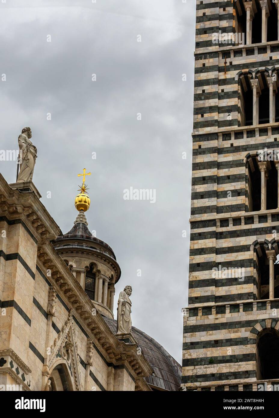 Dettaglio architettonico della Cattedrale di Siena (Duomo), con le sue famose strisce di marmo bianco e nero del campanile, le sculture e una croce d'oro sulla sommità Foto Stock