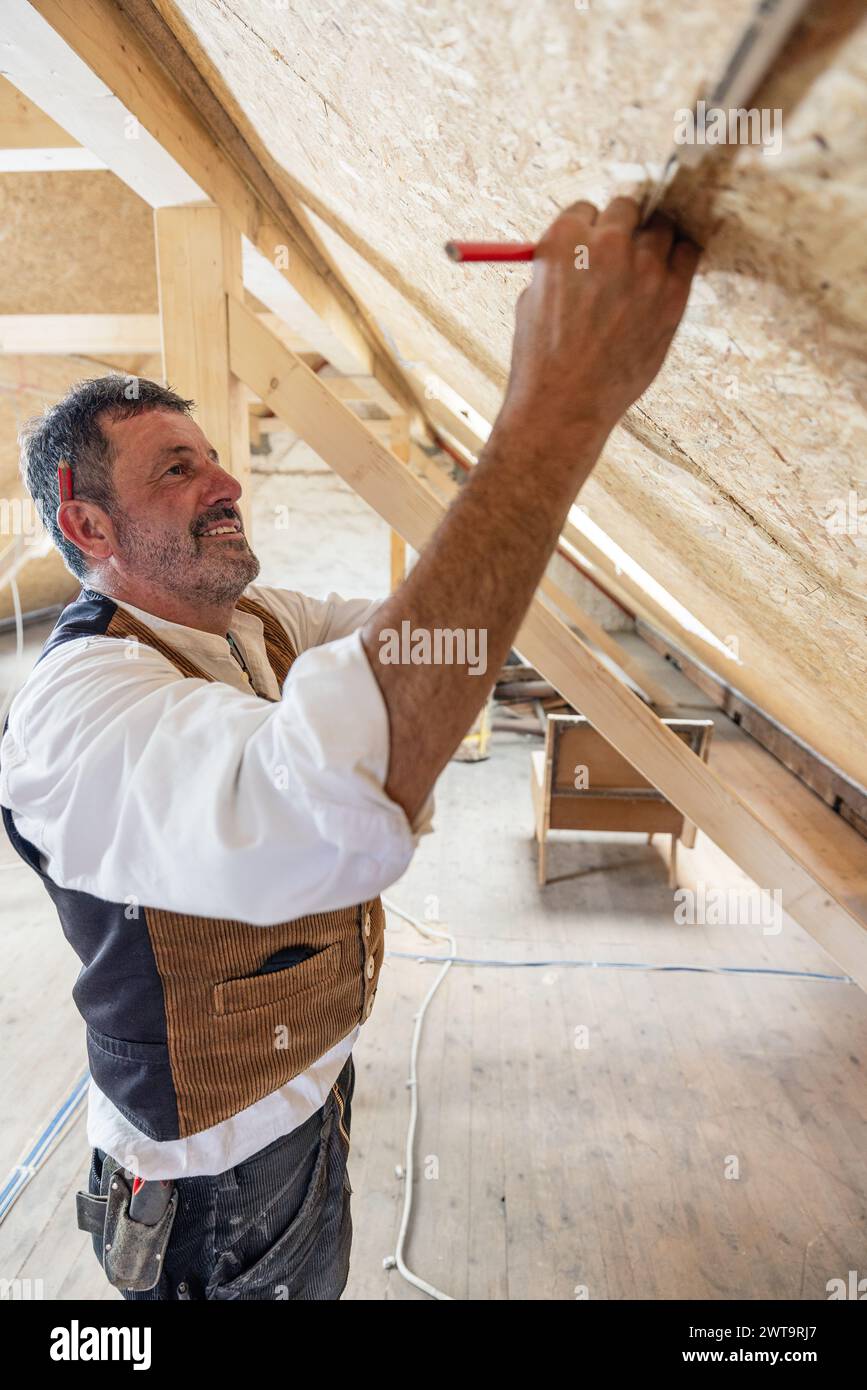 Operaio del legno da costruzione che effettua misurazioni sul sito della conversione dell'attico Foto Stock