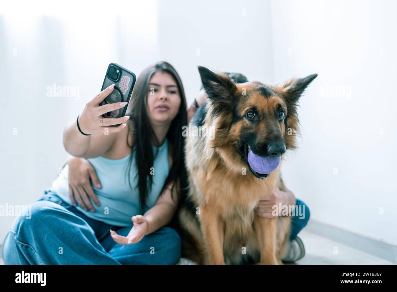 Una coppia latinoamericana rilassata gode di un momento informale con il loro pastore tedesco a casa Foto Stock Una coppia latinoamericana rilassata gode di un momento informale con il loro pastore tedesco a casa Foto Stock