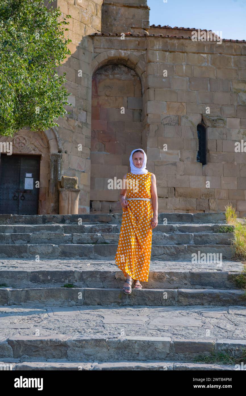 Bella giovane donna in abito arancione e sciarpa bianca in piedi vicino alla vecchia chiesa Foto Stock