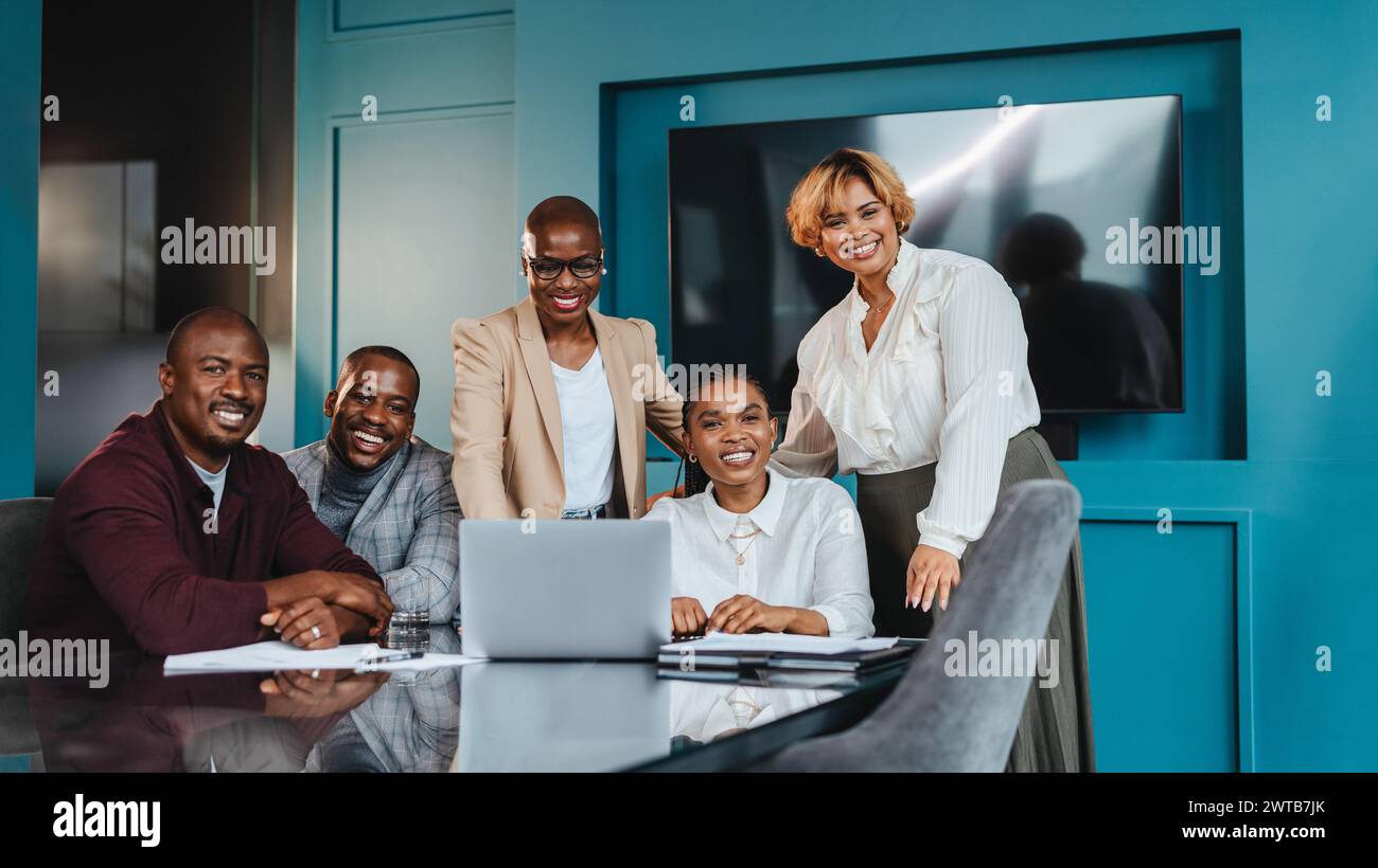 Gruppo di colleghi professionisti impegnati in una riunione aziendale collaborativa in un ufficio a tema blu. Sono riuniti intorno a un notebook, condividendo un'idea Foto Stock