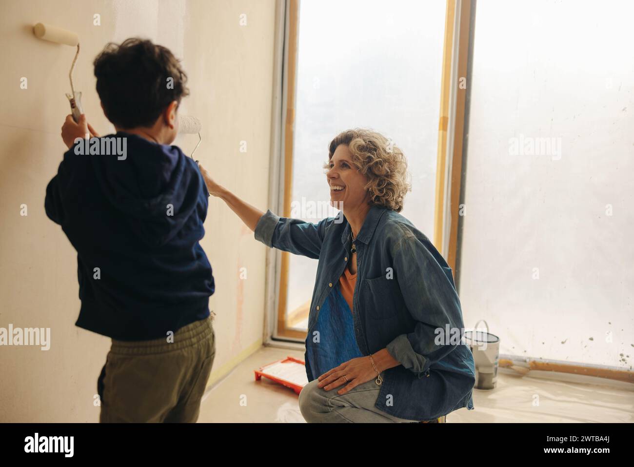 La madre felice e il suo giovane figlio legano mentre dipingono un muro insieme nella loro casa. Apprezzano un progetto di ristrutturazione della casa fai da te, che abbraccia la loro creatività Foto Stock