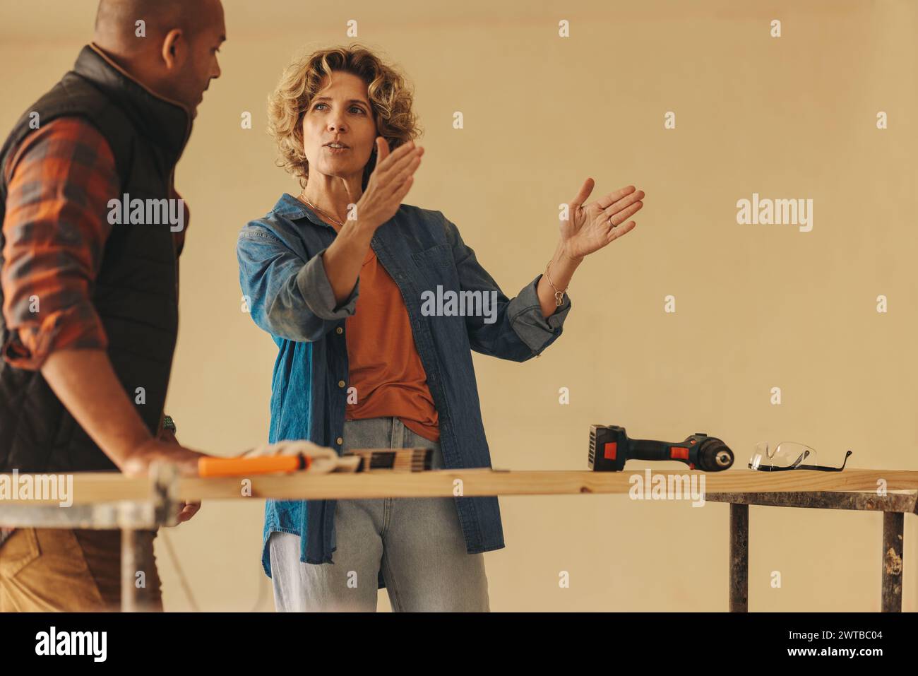 Donna matura che discute con il marito dei piani di ristrutturazione della casa e collabora alla falegnameria fai da te. Pianificano e lavorano insieme, condividendo idee per int Foto Stock