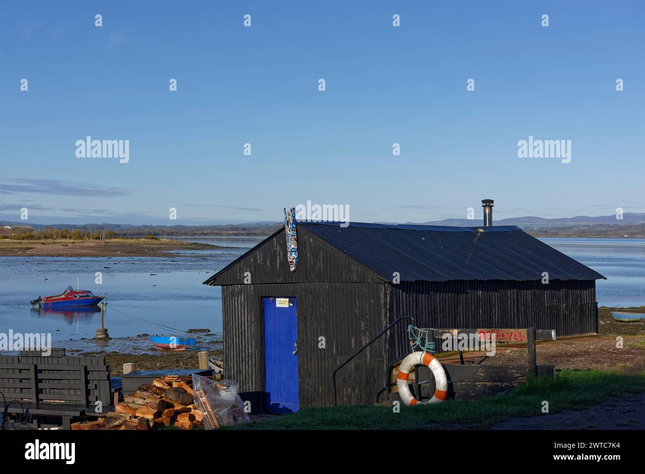 Una piccola capanna dipinta di nero costruita con fogli di latta ondulati con una stufa a legna Chimney che esce dal tetto, a Montrose Basin. Foto Stock