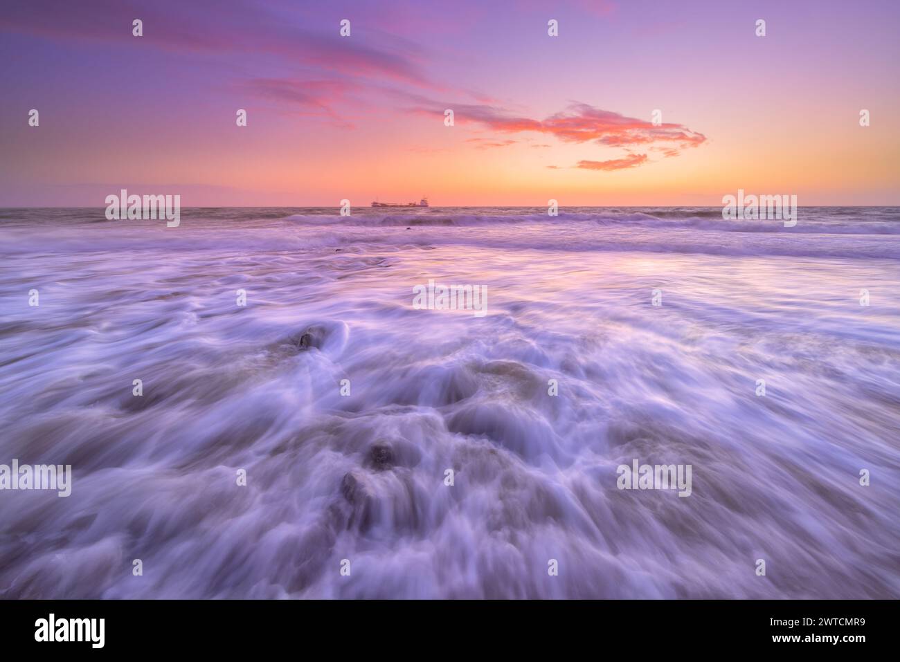 Onde che si infrangono sulla spiaggia dei Paesi Bassi durante un bellissimo tramonto con colori rosa e viola in una tranquilla giornata estiva Foto Stock