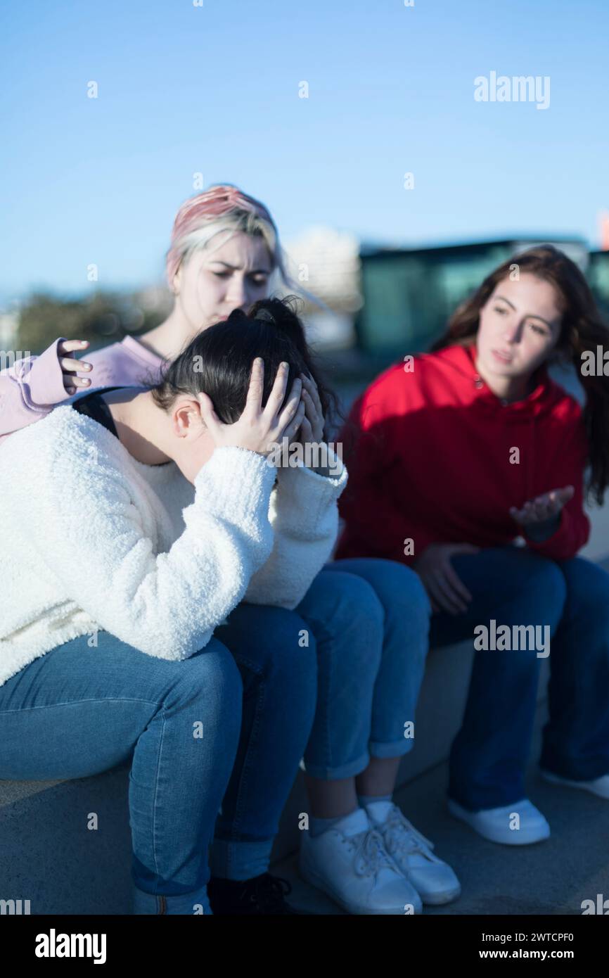 Una donna preoccupata conforta il suo amico in difficoltà, che sta tenendo la testa, mentre un'altra persona gestisce attivamente, partecipando alla discussione Foto Stock