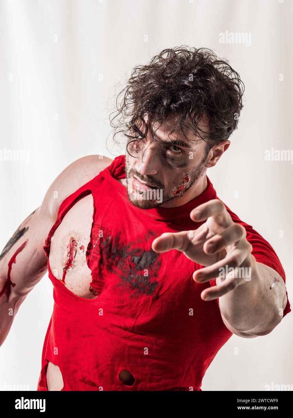 Un uomo zombie che indossa una camicia rossa viene mostrato con il sangue sparso su tutto il corpo. L'immagine cattura una scena di violenza o lesioni, mostrando la messa a fuoco automatica Foto Stock