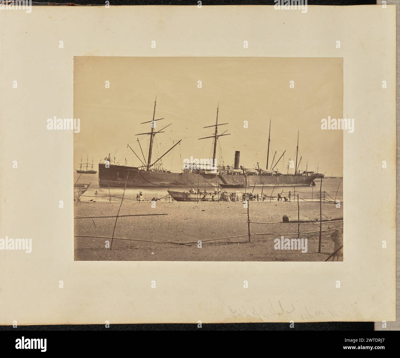 Duca di Sutherland a Madras. Sconosciuto, fotografo gennaio-febbraio 1877 Vista di una grande nave con quattro alberi ormeggiati da una spiaggia. Un certo numero di persone possono essere viste sulla riva, accanto a una barca masula, una tradizionale barca a fondo piatto e dai lati alti, che guarda verso la nave. Una persona sembra usare un ombrello. (Recto, monte) in basso a destra, a matita: "Duca di Sutherland a riva di Madras"; (verso, monte) in basso a sinistra, a matita: "A48.99"; Foto Stock