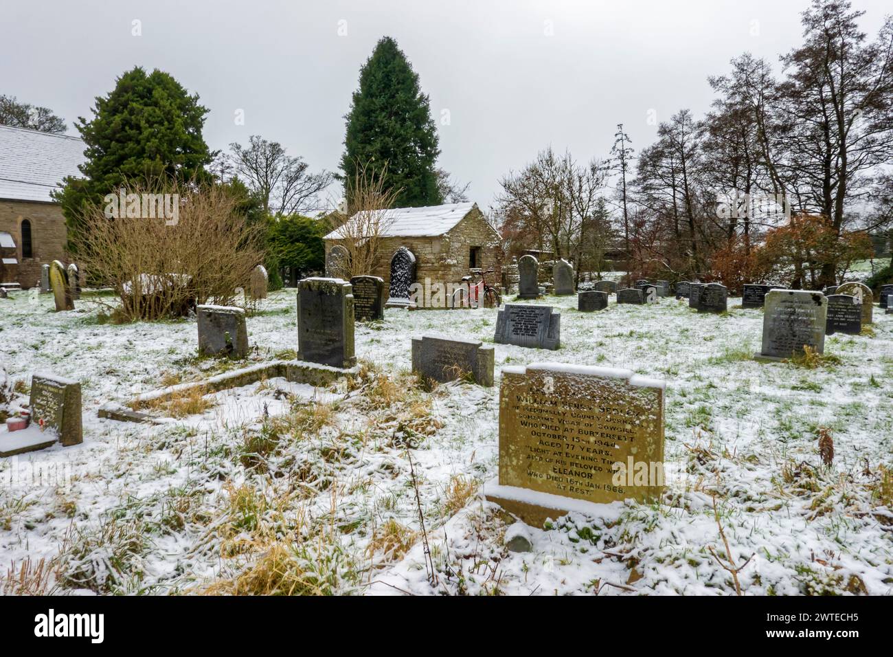 Hardraw Cemetery in una mattina nevosa. Una bicicletta rossa si appoggia contro il capannone di pietra. Foto Stock