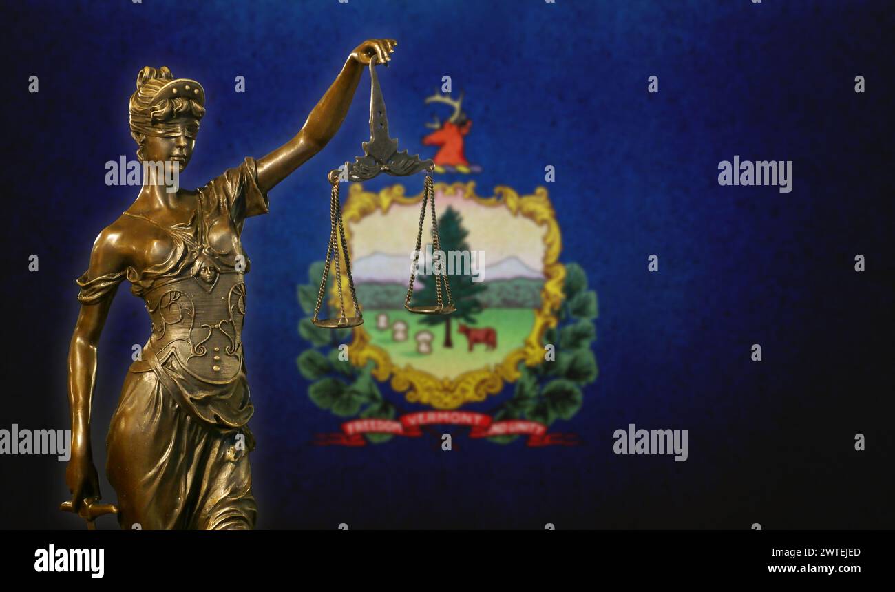 Primo piano di una piccola statuetta di bronzo di Lady Justice davanti a una bandiera del Vermont. Foto Stock