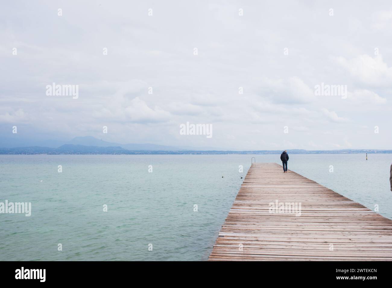 Uomo irriconoscibile in piedi sul molo sul lago di Garda, in Italia Foto Stock
