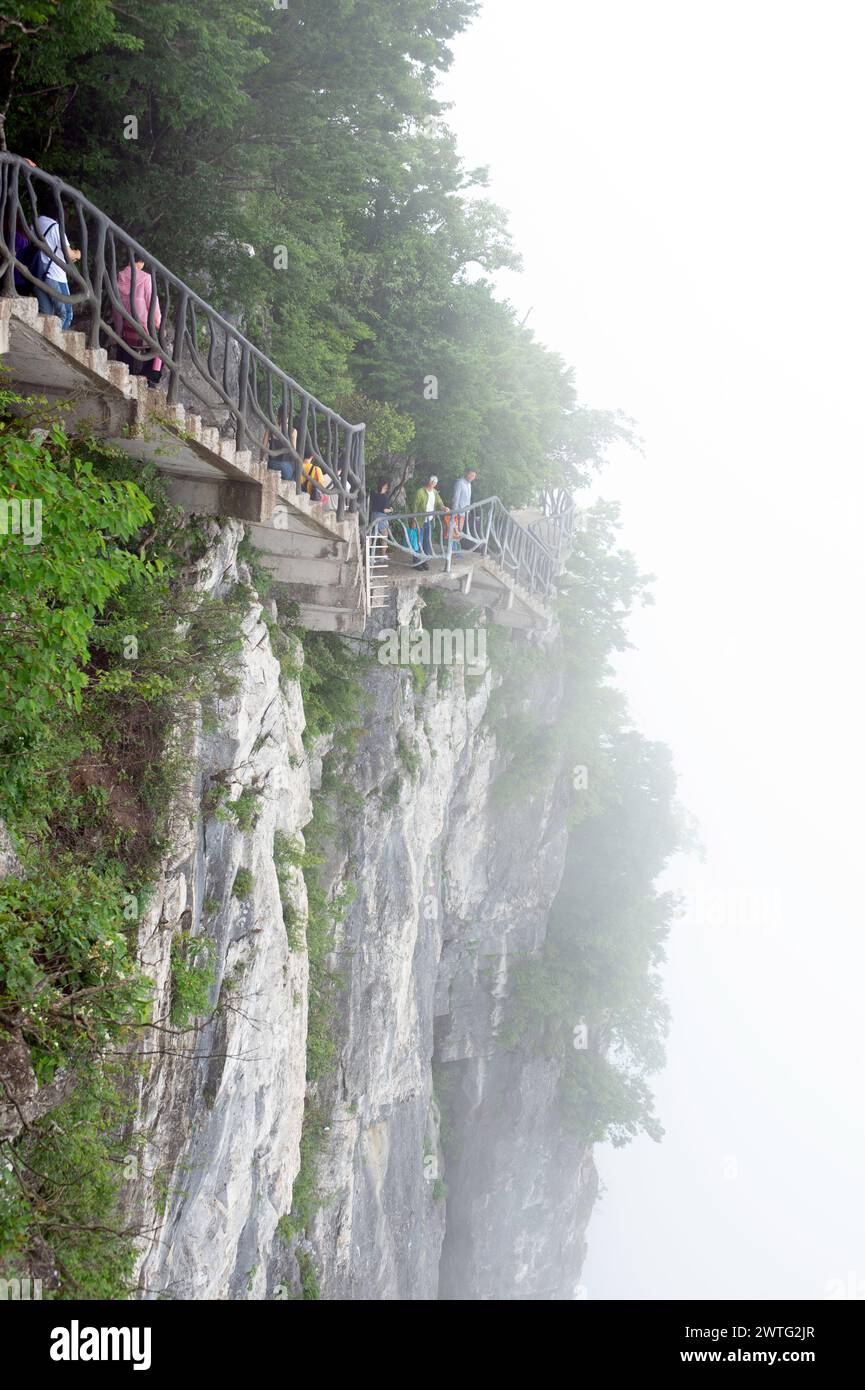 I turisti camminano lungo la Cliff Hanging Walkway, che si aggrappa ai bordi della scogliera verticale delle vette del monte Tianmen. Foto Stock