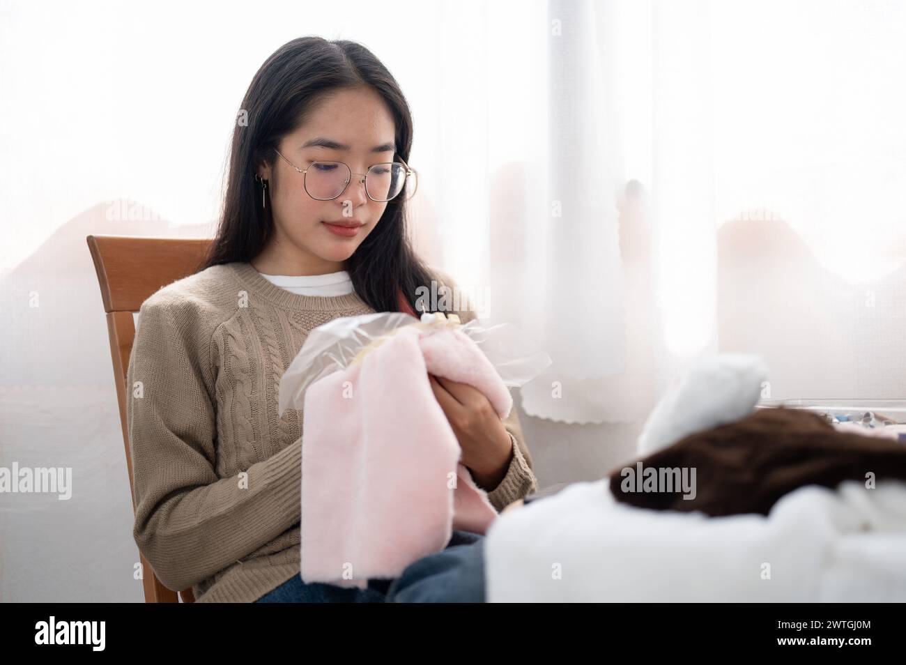 Una bella e tranquilla donna asiatica si concentra sul cucire a mano un motivo su un panno su una cornice da ricamo, creare oggetti fatti a mano, godendosi il suo hobby a hom Foto Stock