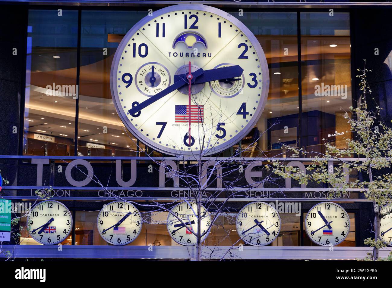 Un grande orologio da parete sulla facciata di un edificio mostra diversi fusi orari ed è adornato con la bandiera americana, Manhattan, New York, New York, USA Foto Stock