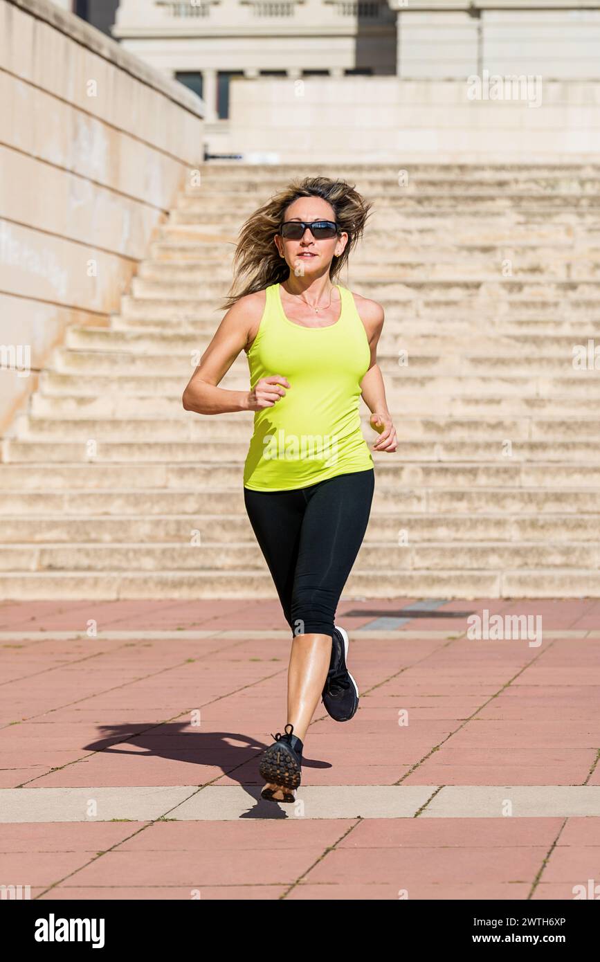 Donna dai capelli lunghi con occhiali da sole che corre in città la mattina. Foto Stock