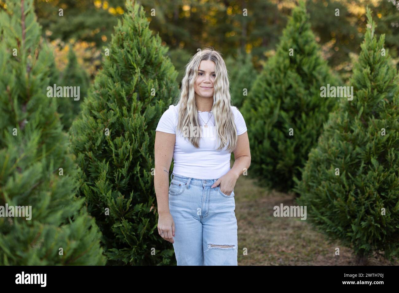 Una donna (33) in tee bianco e jeans blu, in una fattoria di alberi di Natale Foto Stock