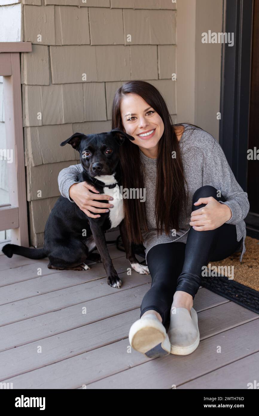 Una donna radiosa e il suo fedele cane si godranno un momento di relax in una veranda di casa Foto Stock