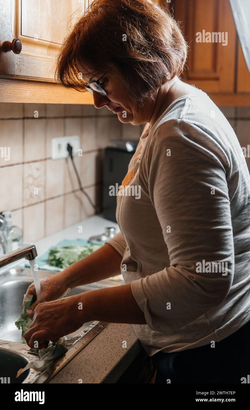 Una donna prepara un pasto di famiglia lavando lattuga in una cucina accogliente Foto Stock