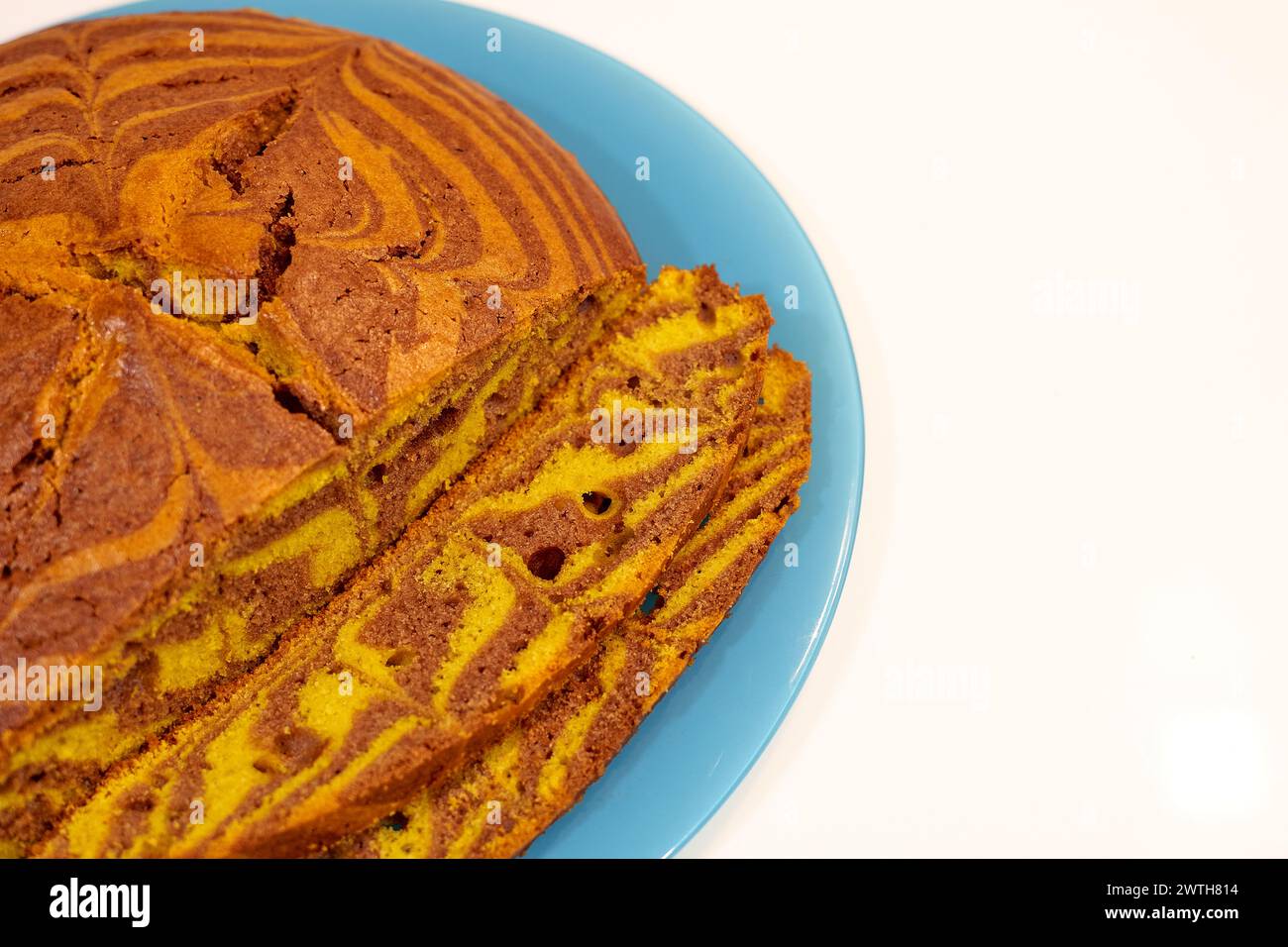 Una fetta di torta con un piatto blu su sfondo bianco. La torta viene tagliata a pezzi e presenta una stampa zebra Foto Stock