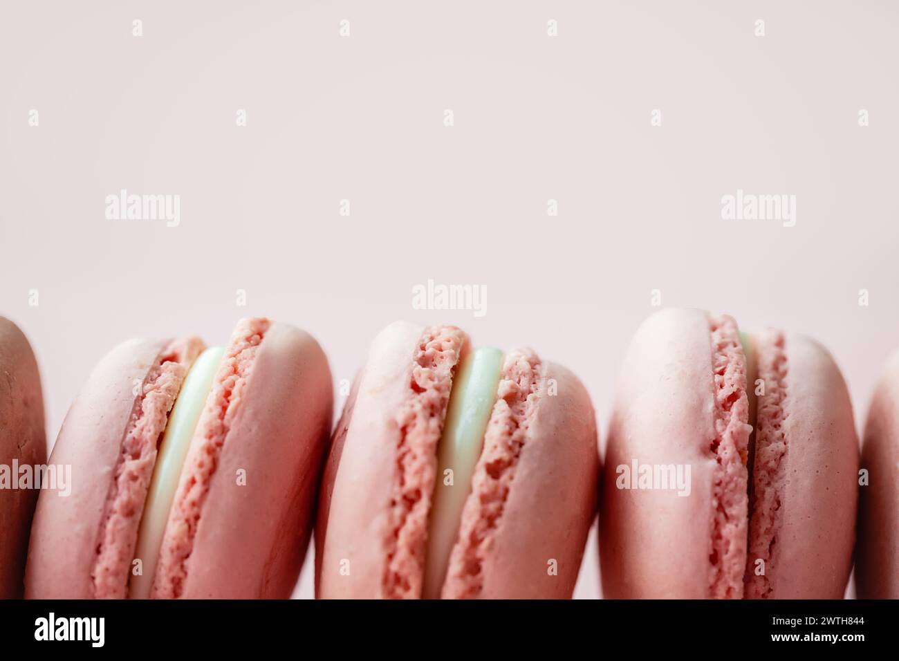 Primo piano di macaron di fila su una superficie rosa pallida Foto Stock