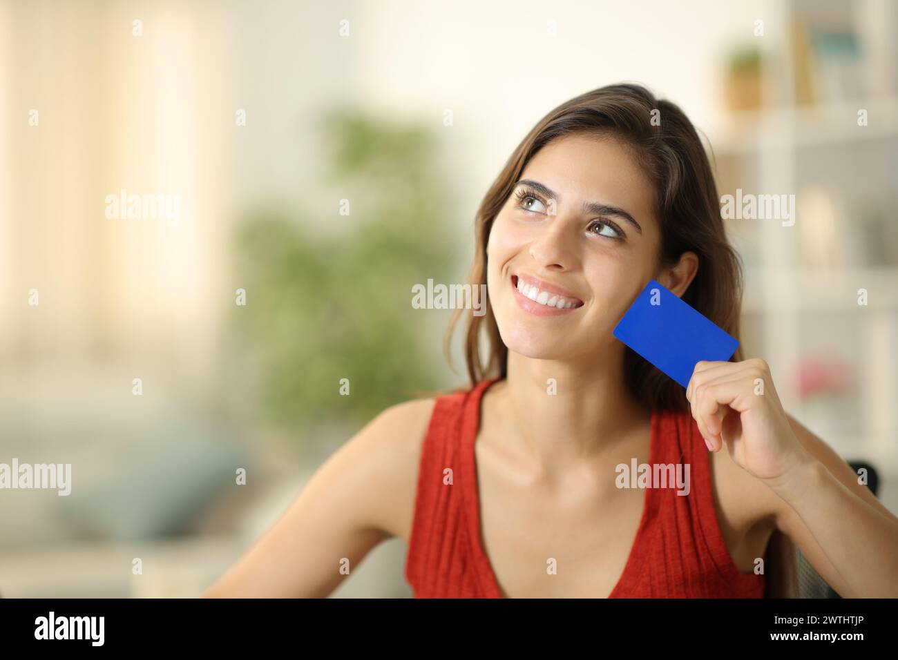 Donna felice che sogna e mostra una carta di credito vuota a casa Foto Stock
