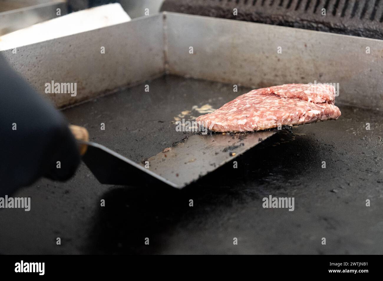 Schwabmünchen, Baviera, Germania - 17 marzo 2024: Lo chef prepara un hamburger di carne macinata cruda su una griglia gastronomica *** Koch legt einen rohen Hackfleisch Burger Patty auf einen gastronomie Grill Foto Stock