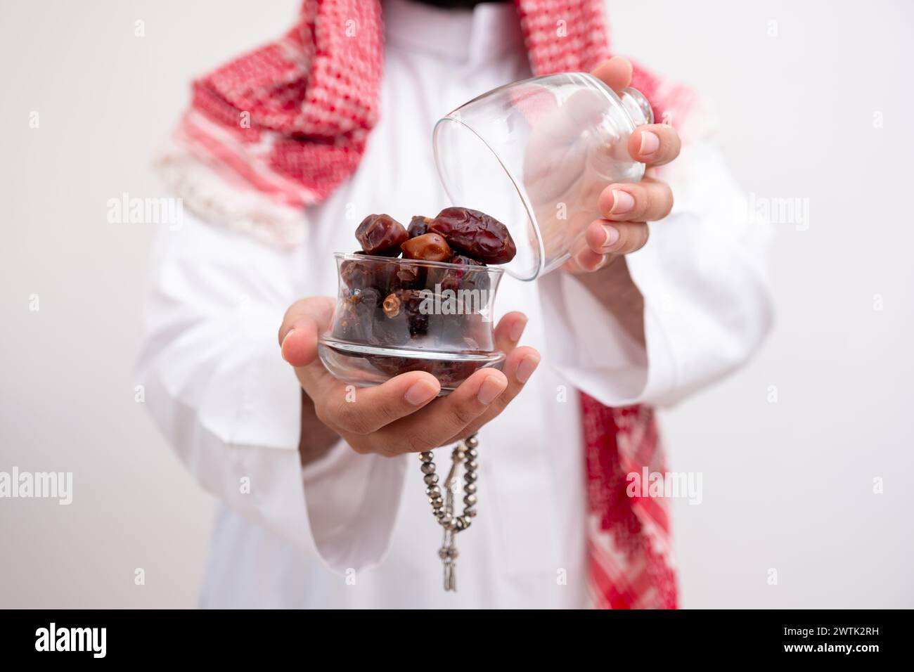 l'uomo arabo che tiene datteri rappresenta ospitalità e generosità indossando kandura con keffiyeh su sfondo bianco isolato per le celebrazioni eid Foto Stock