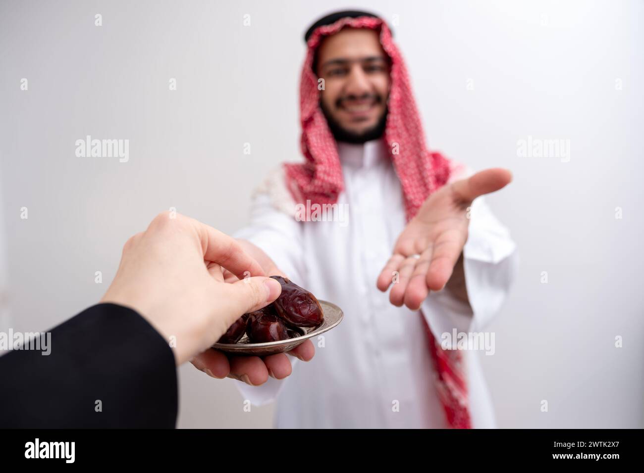 l'uomo arabo che tiene datteri rappresenta ospitalità e generosità indossando kandura con keffiyeh su sfondo bianco isolato per le celebrazioni eid Foto Stock