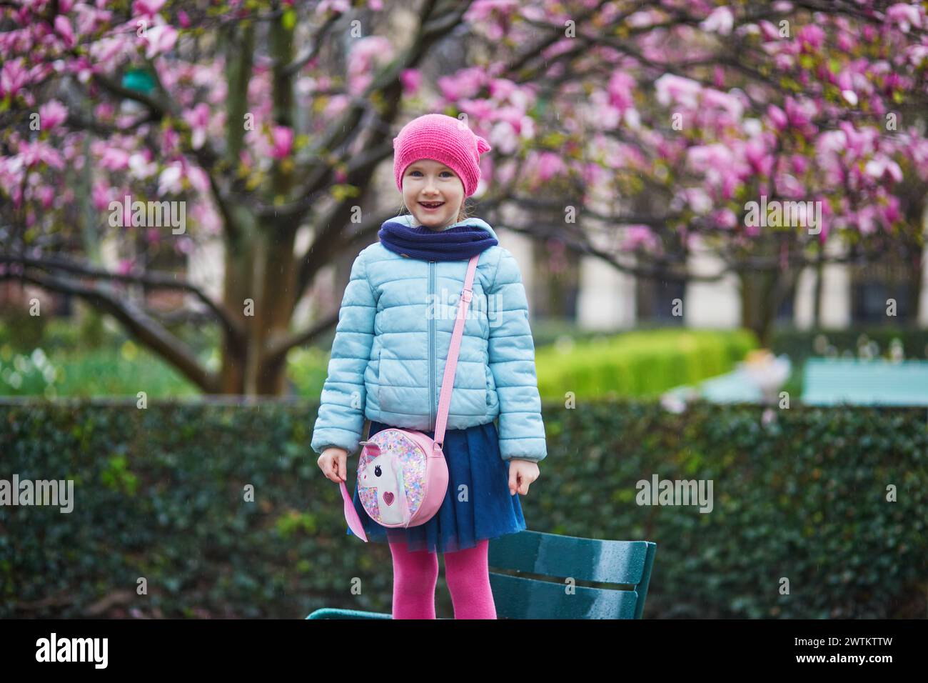 Adorabile ragazza in età prescolare che si gode di magnolie rosa in piena fioritura in una giornata di pioggia in un parco di Parigi, Francia Foto Stock