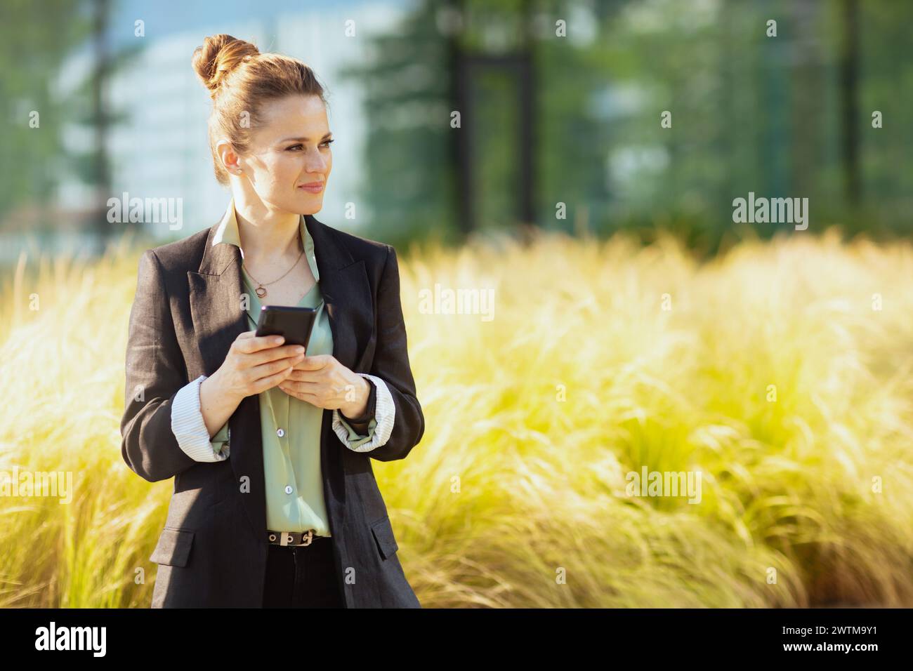 lavoratrice moderna felice nel quartiere degli affari con giacca nera che utilizza lo smartphone. Foto Stock