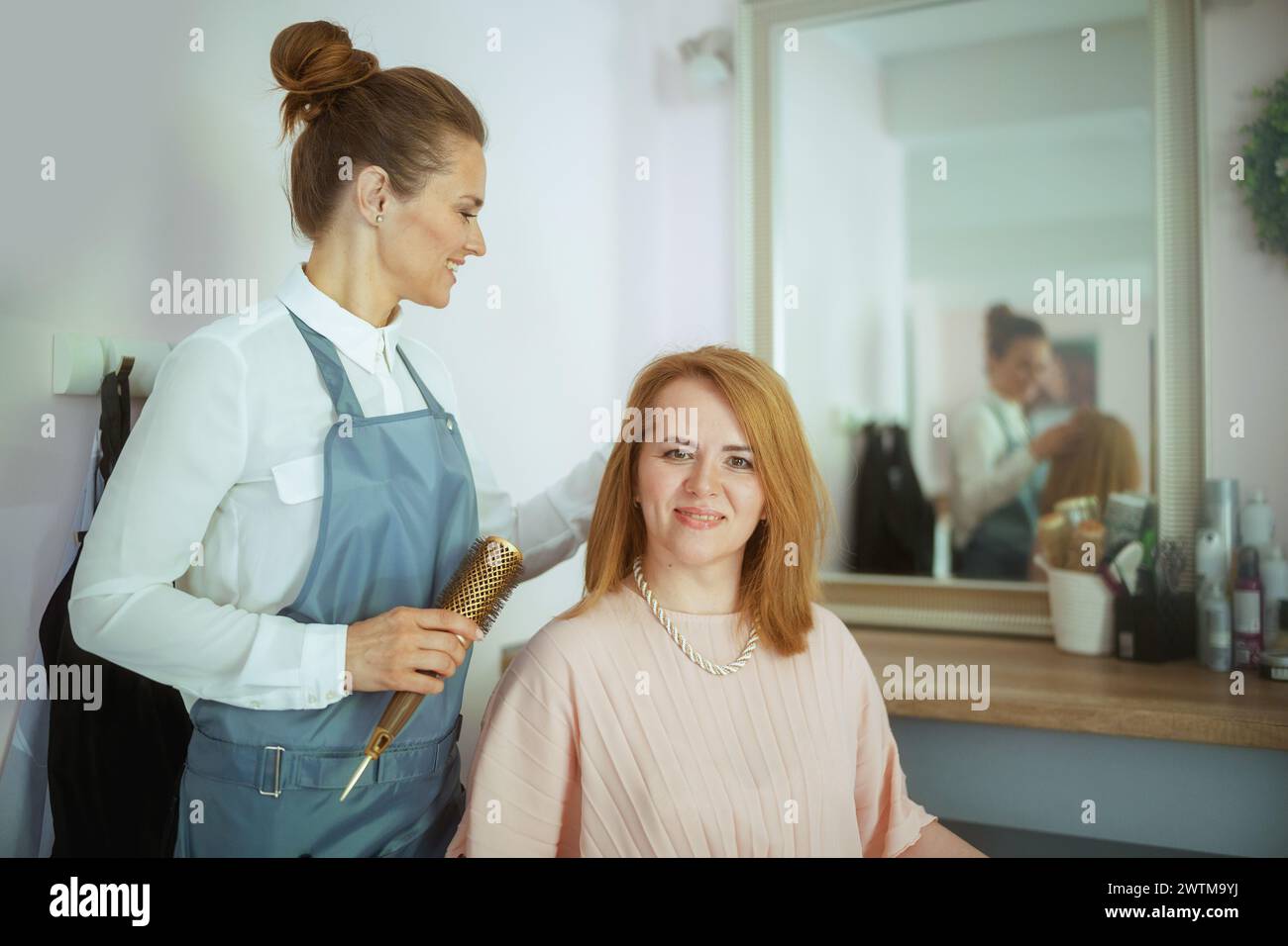 parrucchiere di mezza età in un moderno salone di bellezza con spazzola per capelli e cliente. Foto Stock