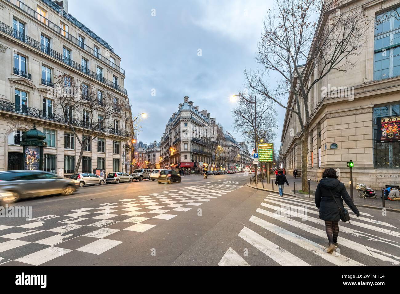 I pedoni attraversano al crepuscolo per le vivaci strade di Parigi con l'architettura classica che costeggia il viale. Foto Stock