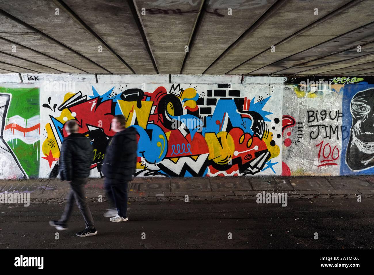 La gente passa davanti a un murale di graffiti sotto un ponte a Glasgow, in Scozia. Foto Stock