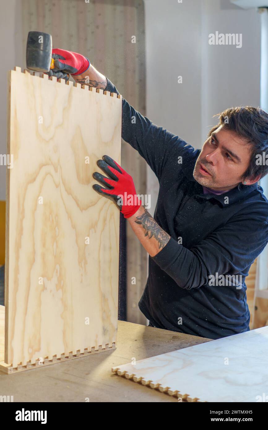 Falegname ispanico di mezza età che lavora in piedi nella sua falegnameria assemblando un pezzo di mobili Foto Stock