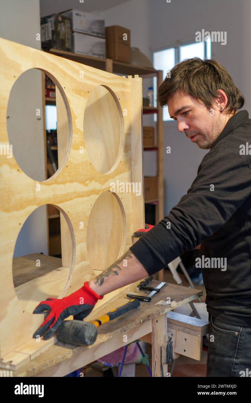 Falegname ispanico di mezza età che lavora in piedi nella sua falegnameria assemblando un pezzo di mobili Foto Stock
