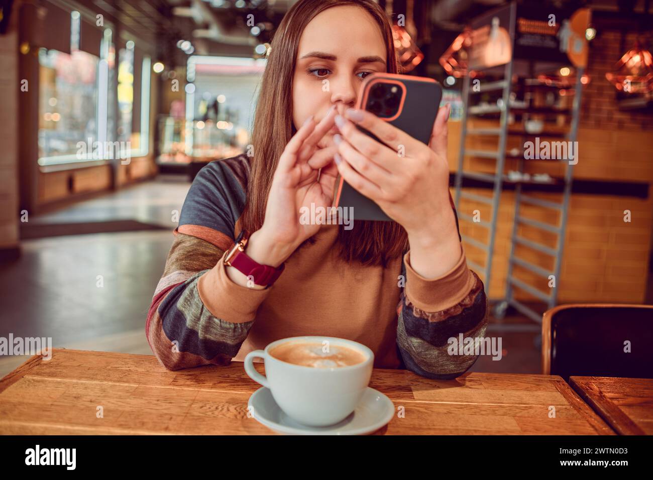 Una donna sfoglia intensamente il suo telefono, una tazza di caffè nelle vicinanze, nell'atmosfera invitante di un caffè locale Foto Stock