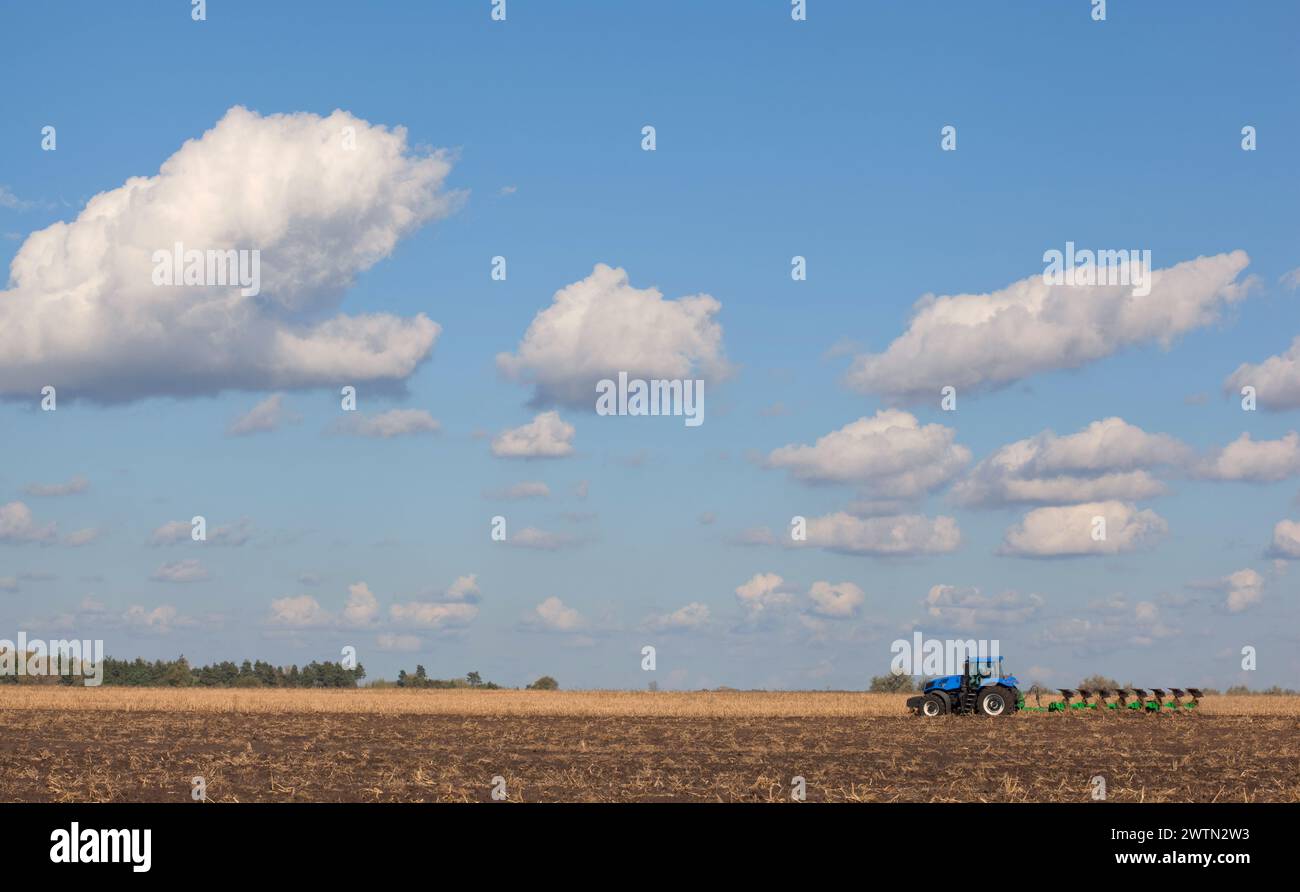 un grande trattore blu, che ara il campo contro il cielo. Lavori di macchine agricole. Raccolto Foto Stock