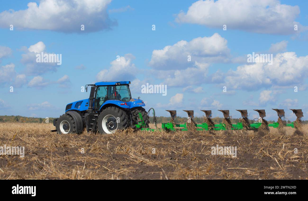 un grande trattore blu, che ara il campo contro il cielo. Lavori di macchine agricole. Raccolto Foto Stock