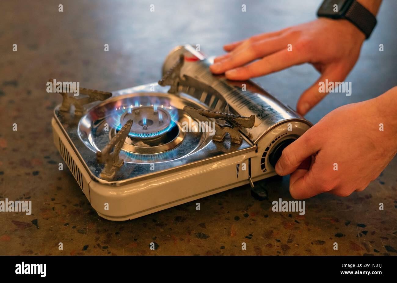 Stile di vita attivo. La mano di un uomo accende una stufa a gas portatile. Una fonte alternativa per cucinare a casa durante un'interruzione di corrente Foto Stock