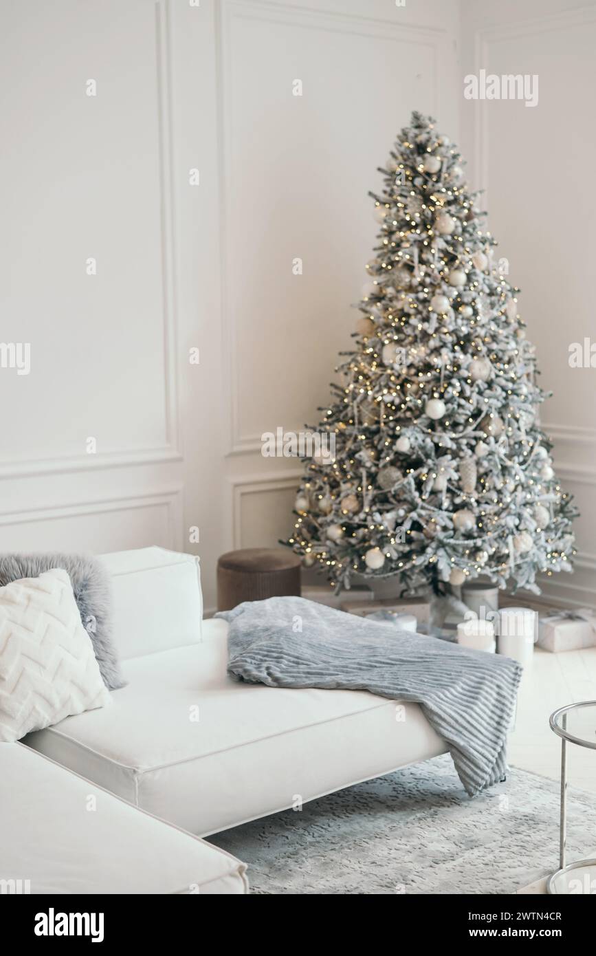 Decorazioni natalizie in uno studio fotografico in grigio e bianco. Albero di Natale bianco neve, regali e lanterne, divano. fuori fuoco. Spazio per un servizio fotografico Foto Stock